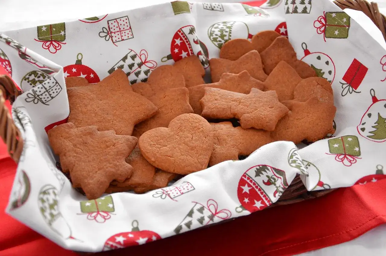 Cesto pieno di biscotti alla cannella a forma di stella, cuore e albero, su un telo natalizio.