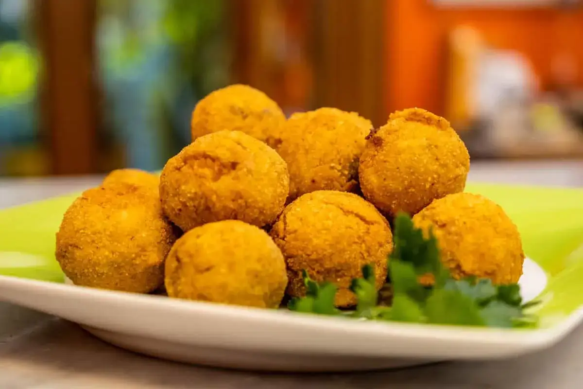 Un mucchio di dorate polpette di pesce, croccanti fuori e morbide dentro, servite su un piatto verde con un ciuffo di prezzemolo.