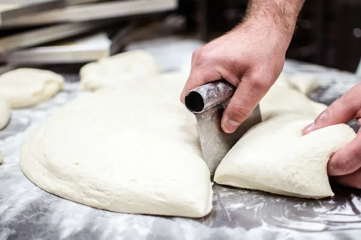 Mani esperte dividono l'impasto pizza napoletana, pronto per lievitare e diventare una delizia.