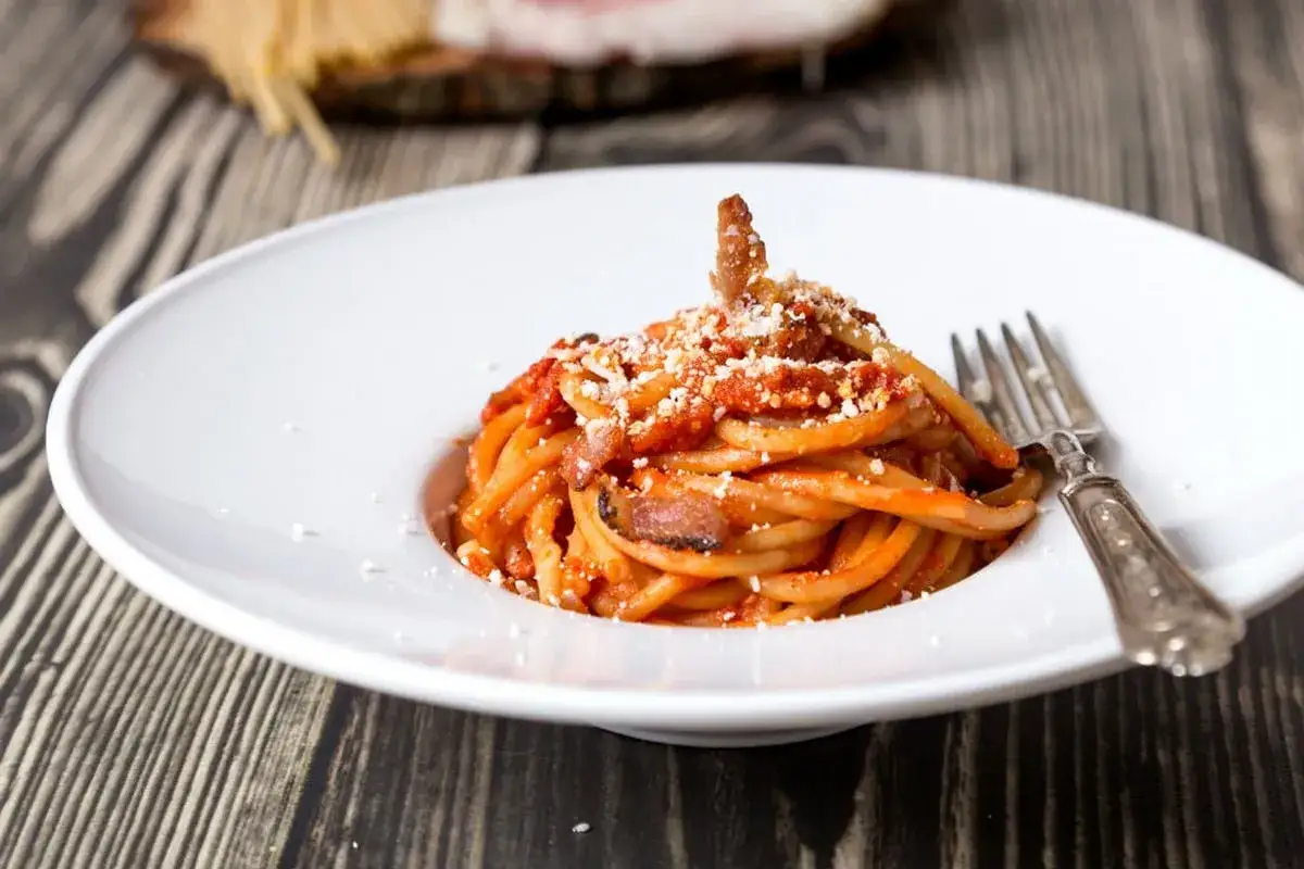Un piatto di bucatini all'amatriciana ricetta originale, conditi con sugo rosso e guanciale croccante, spolverati di pecorino.