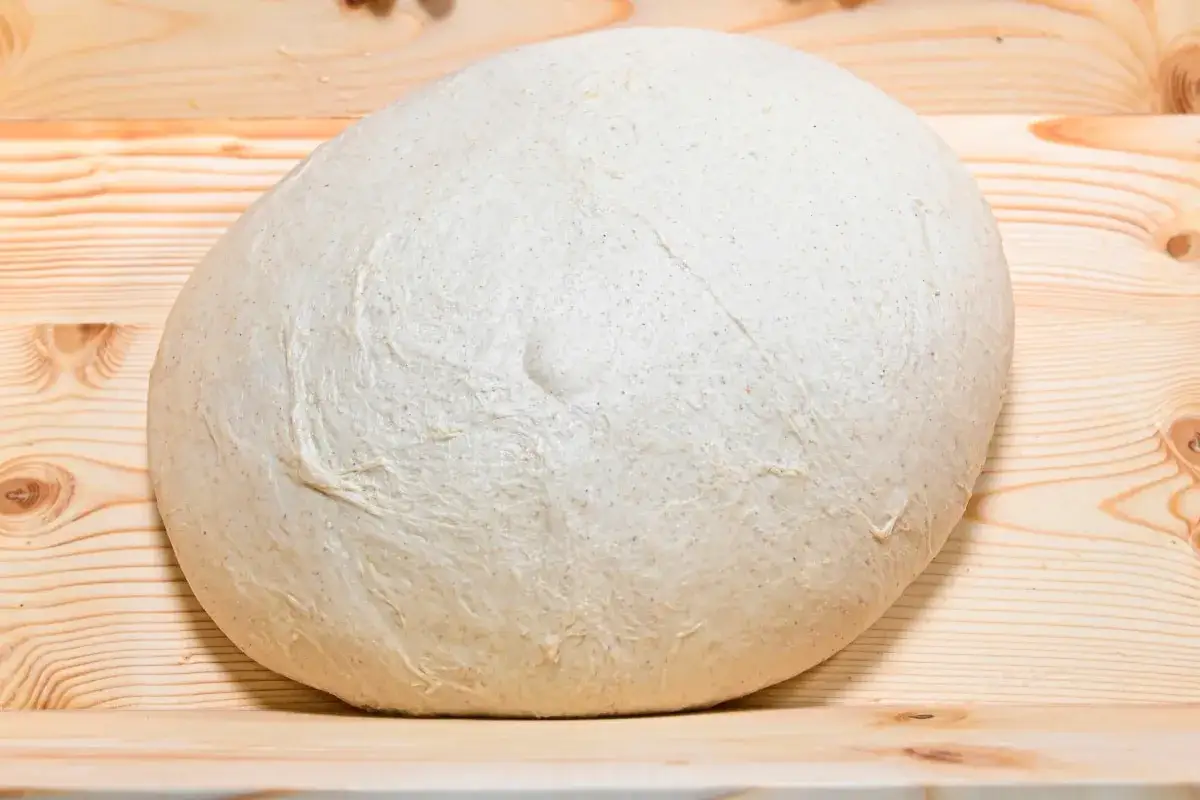 Impasto per pizza soffice e lievitato, pronto per essere steso su un tagliere di legno.