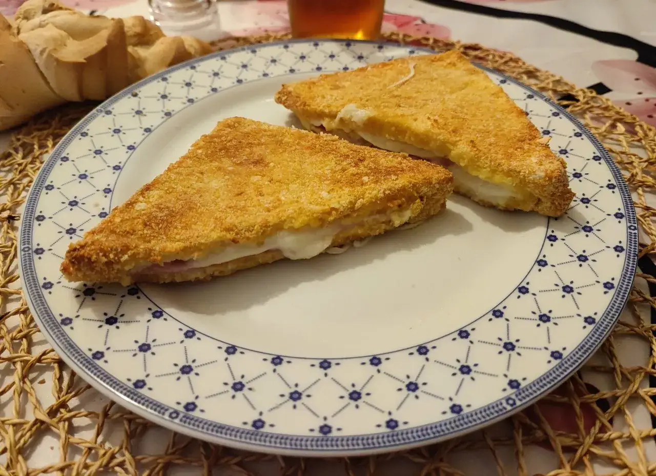 Due triangoli dorati di mozzarella in carrozza, cotti in friggitrice ad aria, su un piatto con bordo blu.