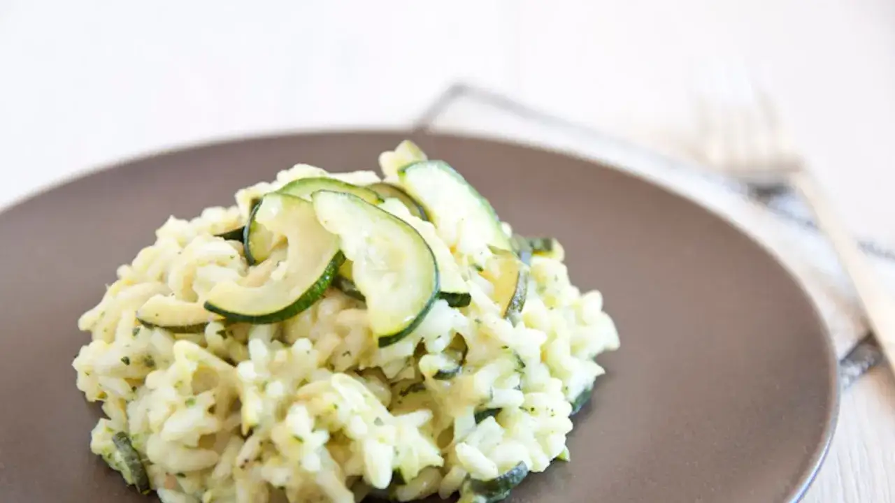 Un cremoso risotto con zucchine, guarnito con fette sottili di zucchine fresche. Un piatto leggero e saporito.