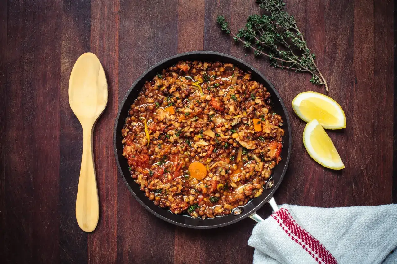 Un saporito ragù di lenticchie in padella, pronto per essere gustato con un cucchiaio di legno. Accompagnato da limone e timo fresco.