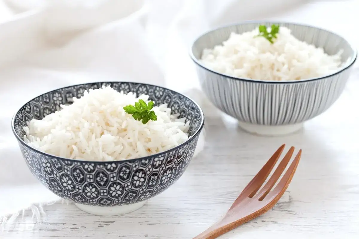 Due ciotole piene di riso in bianco, guarnite con prezzemolo. Un cucchiaio di legno è pronto per gustare questo piatto semplice e delizioso.