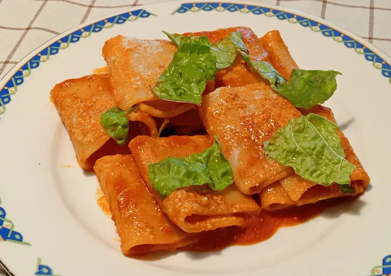 Paccheri alla Vittorio, un piatto invitante con pasta condita in salsa rossa e guarnita con foglie verdi fresche.
