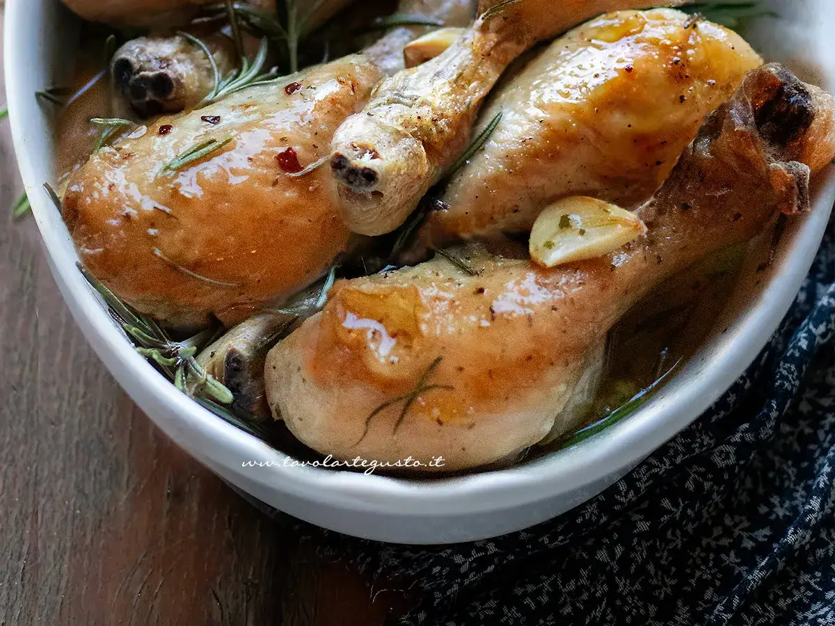 Succulenti fusi di pollo cotti al forno con aglio e rosmarino, serviti in una ciotola bianca.
