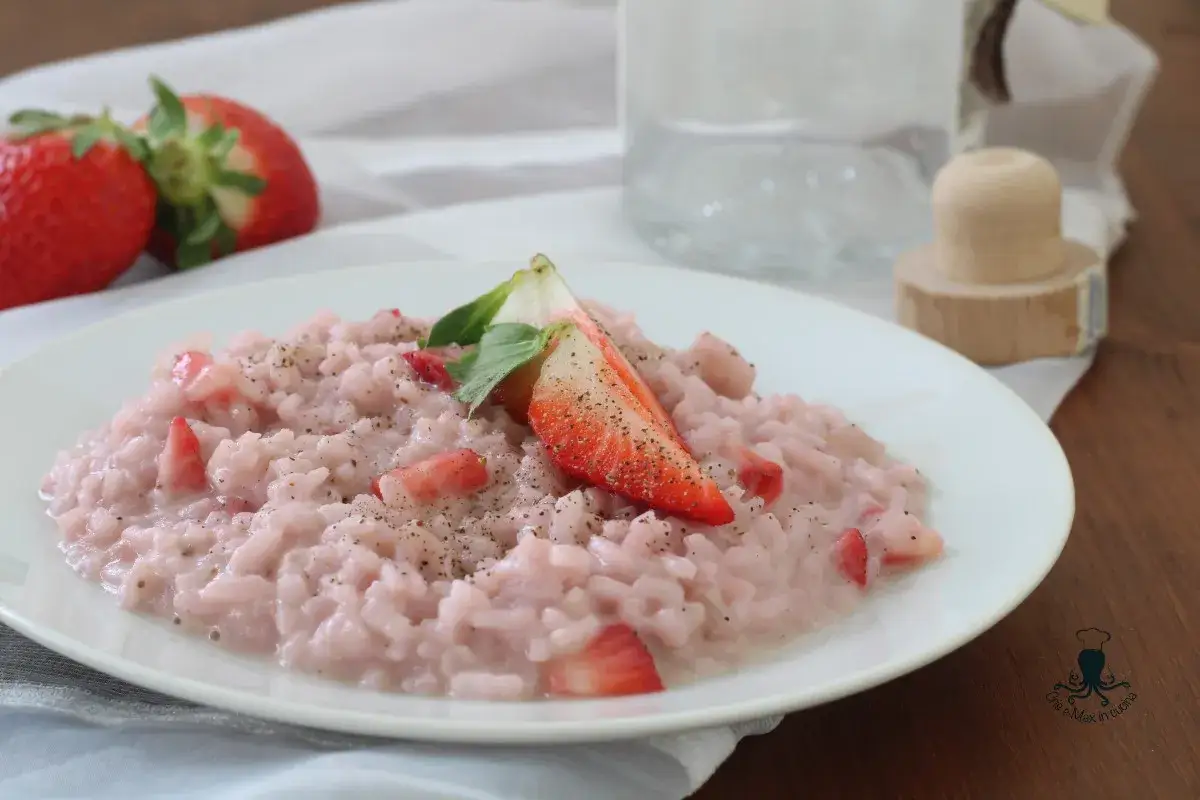 Un cremoso risotto alle fragole, guarnito con fragole fresche e pepe nero, su un piatto bianco.