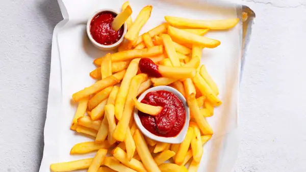 Patatine fritte dorate e croccanti con due ciotoline di ketchup fatto in casa, una con una patatina che si tuffa dentro.