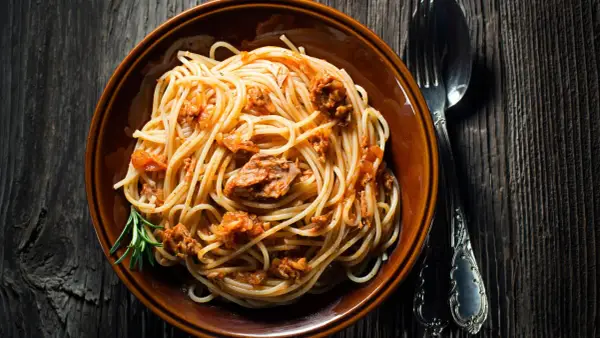 Un piatto di spaghetti al tonno, conditi con un sugo saporito e guarniti con un rametto di rosmarino, pronti per essere gustati.