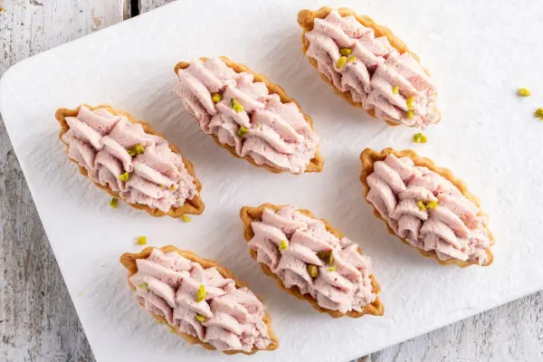 Piccoli cestini di pasta brisée ricetta, ripieni di crema rosa e guarniti con pistacchi.