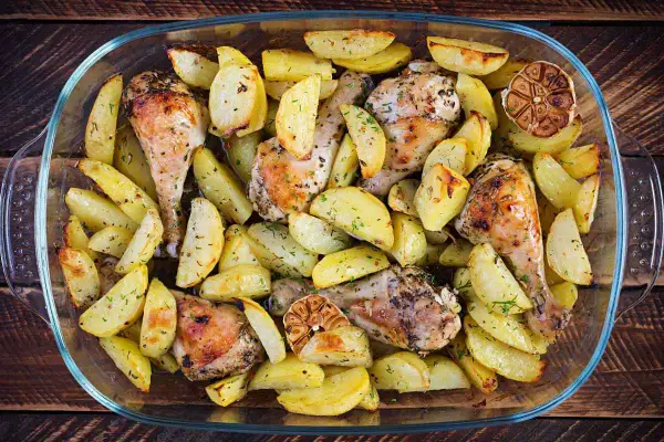 Un succulento pollo e patate al forno, dorati e profumati, in una teglia di vetro.